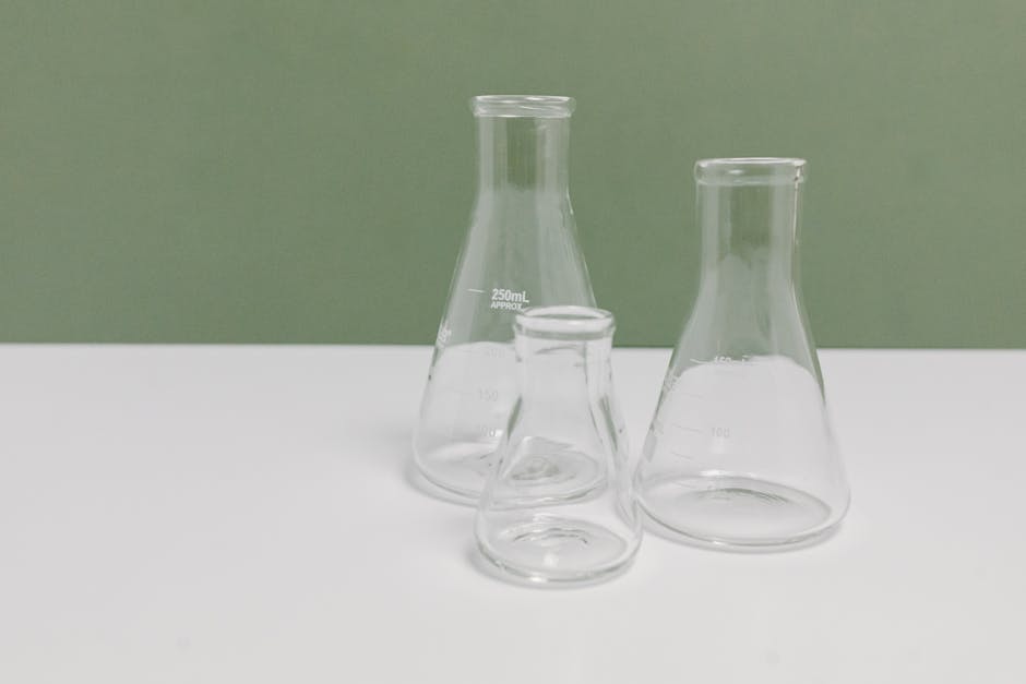 A set of three clear glass laboratory flasks on a clean white and green background, ideal for science themes.