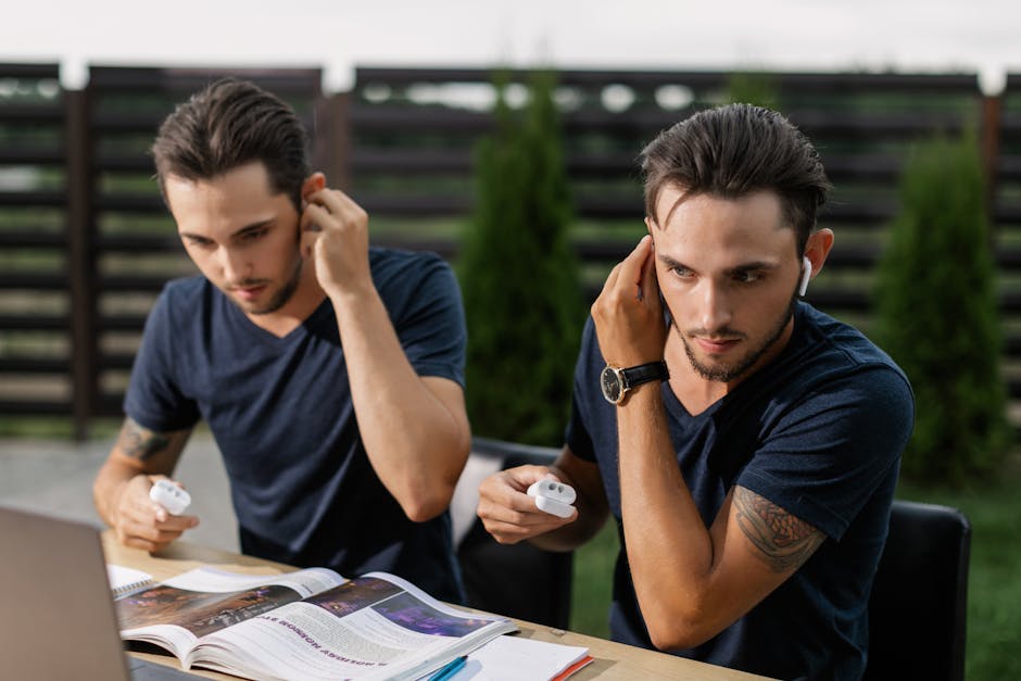 Twin brothers studying outdoors, using wireless earbuds with a laptop.