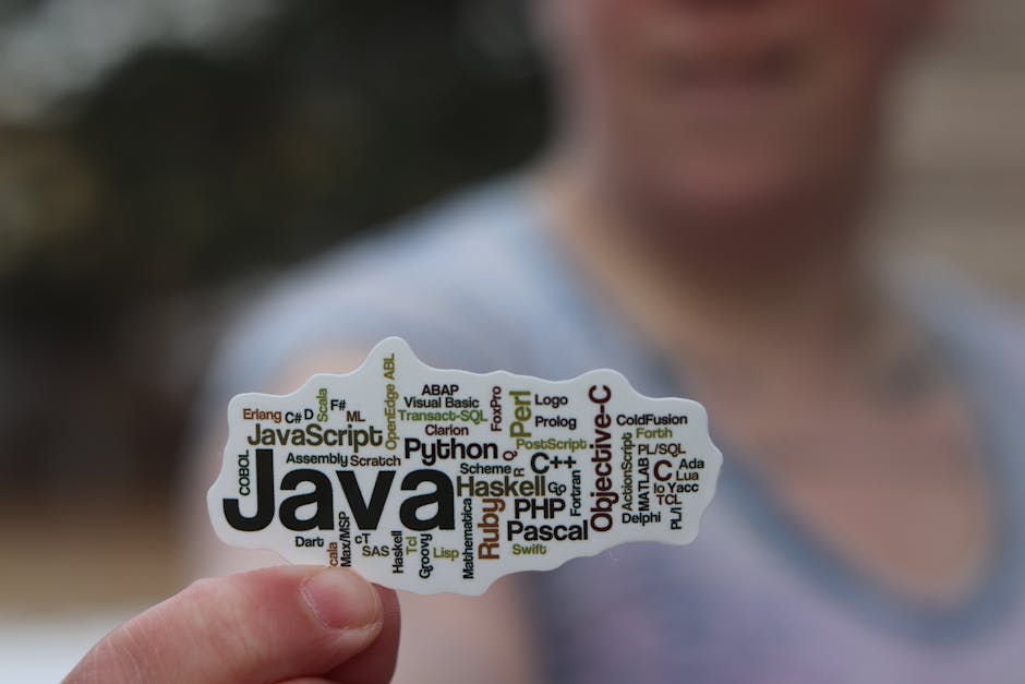 Close-up of a person holding a sticker with various programming languages listed on it.