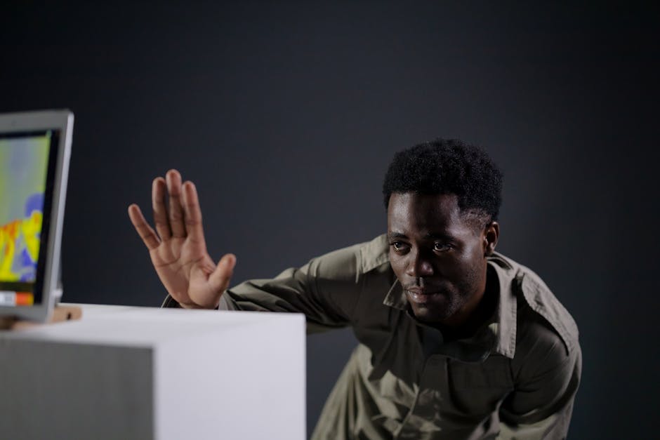 A man interacts with a thermal imaging screen in a dimly lit space, raising his hand.