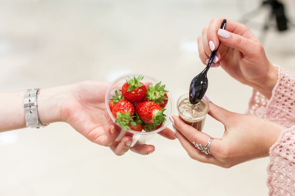 Close-up of hands holding fresh strawberries and a chocolate dessert cup with a spoon.