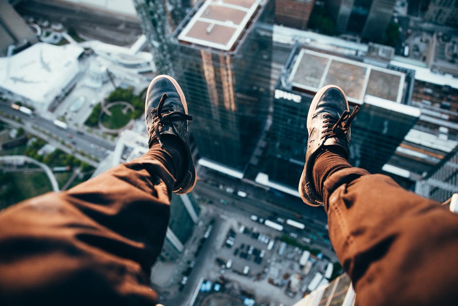 Exhilarating rooftop view of cityscape below with legs dangling from edge.