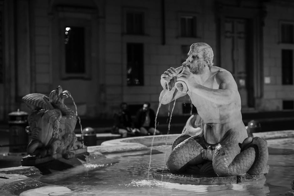 Black and white photo of Triton Fountain statue in Rome's cityscape at night.