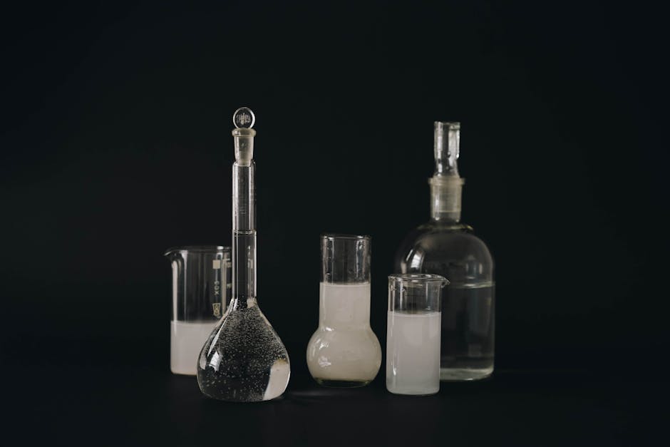 Set of glass laboratory bottles and flasks with liquids on a dark background.