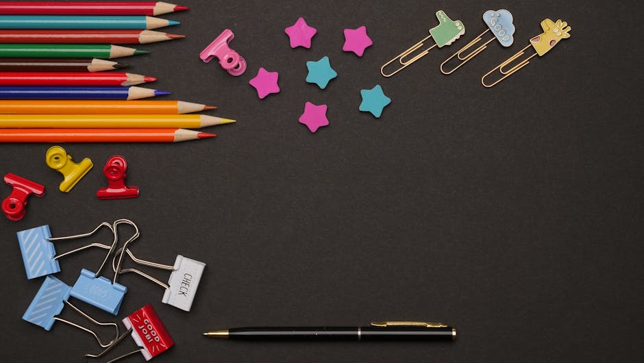A vibrant flat lay of art supplies on a dark backdrop, featuring pencils and paper clips.
