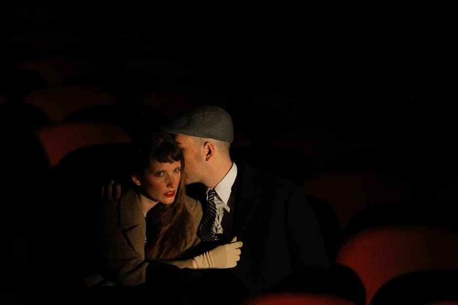 A couple in love whispers in a dimly lit cinema, evoking a sense of intimacy and vintage allure.