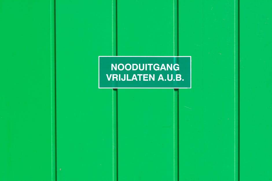 A green metal wall featuring an emergency exit sign in Dutch. Perfect for safety-themed graphics.