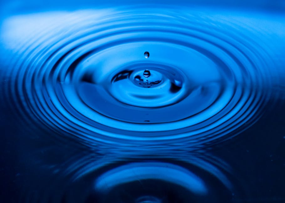 Captivating image of a blue water drop creating ripples on the surface, showcasing nature's beauty.