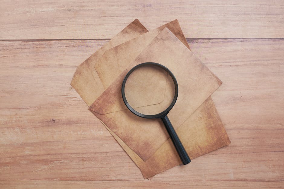 Close-up of a black magnifying glass on aged papers on a wooden surface, offering a classic flat lay composition.