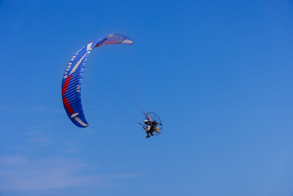 A person flies a paramotor under a clear blue sky in Sam Roi Yot, Thailand.