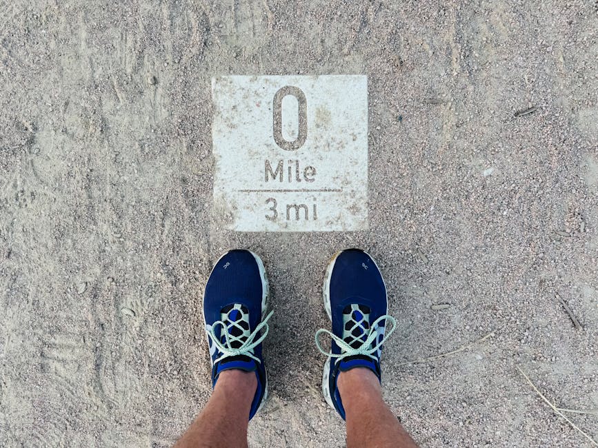 Close-up shot of blue running shoes at a 0 mile marker on a dusty path, symbolizing a journey's start.