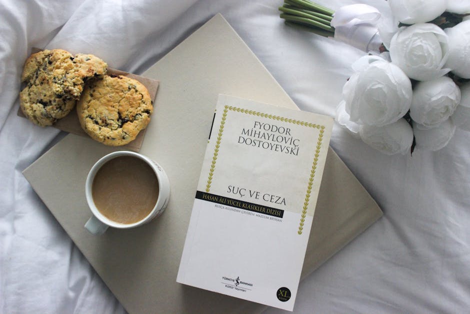 Top view of a book, coffee, and cookies on a bed with white roses.