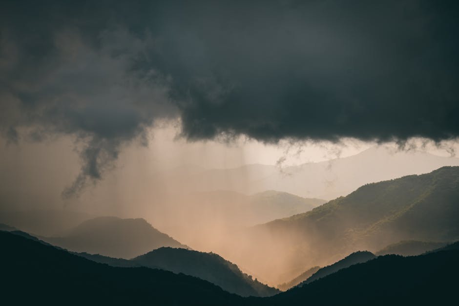 A breathtaking view of storm clouds over a mountain range, casting sun rays.