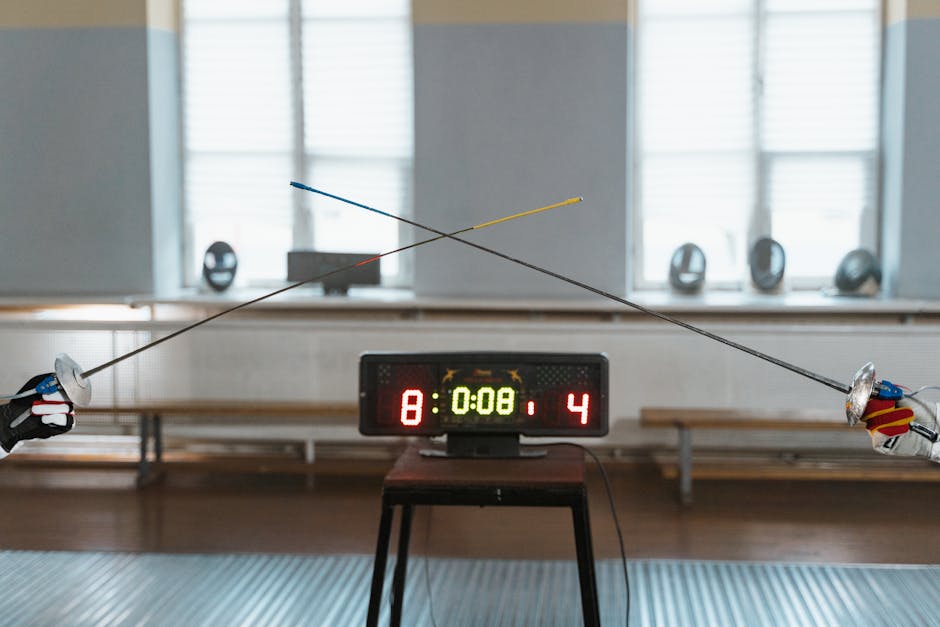 Two fencers engaged in a duel with the scoreboard showing 8:4 indoors.