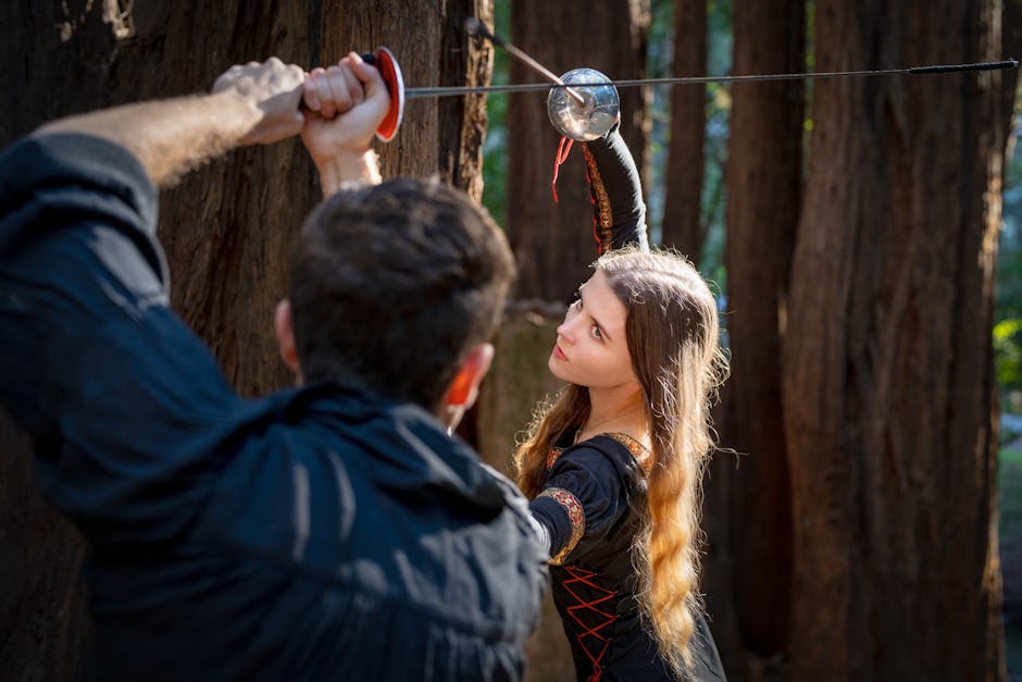 A man and woman engage in a historical sword duel in the woods.