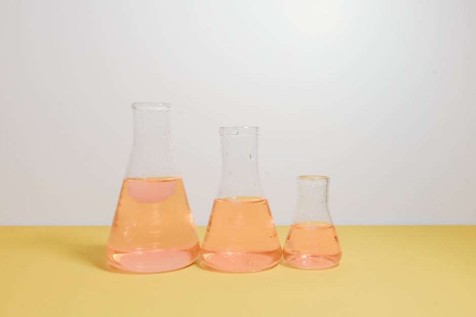Three Erlenmeyer flasks filled with pink liquid on a yellow surface in a lab setting.