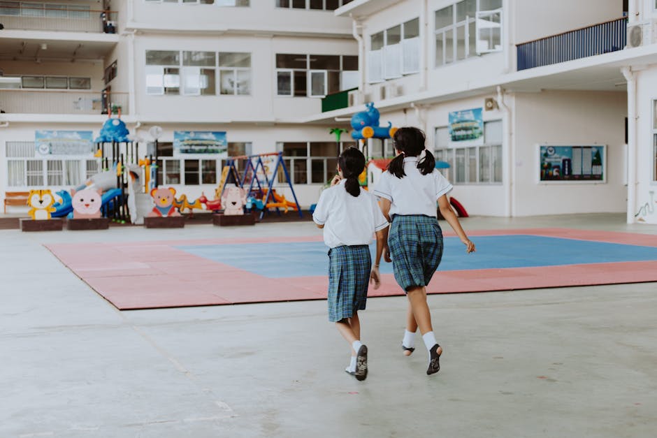 Two girls in school uniforms walking inside a gymnasium with playful decor.