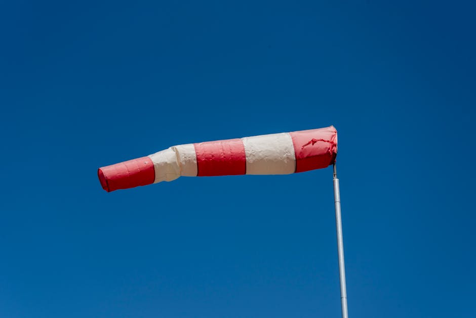 Vibrant red and white windsock blown by the wind against a clear blue sky.