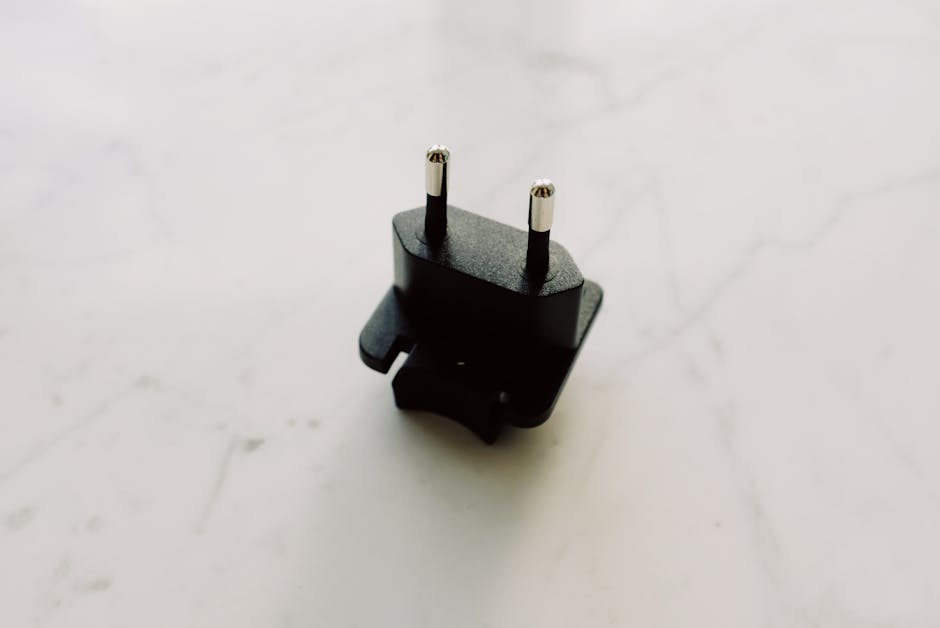 A close-up view of a black electrical adapter on a white marble surface.