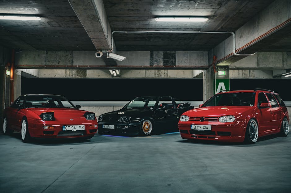A group of three stylish sports cars parked under ambient lighting in an urban garage setting.
