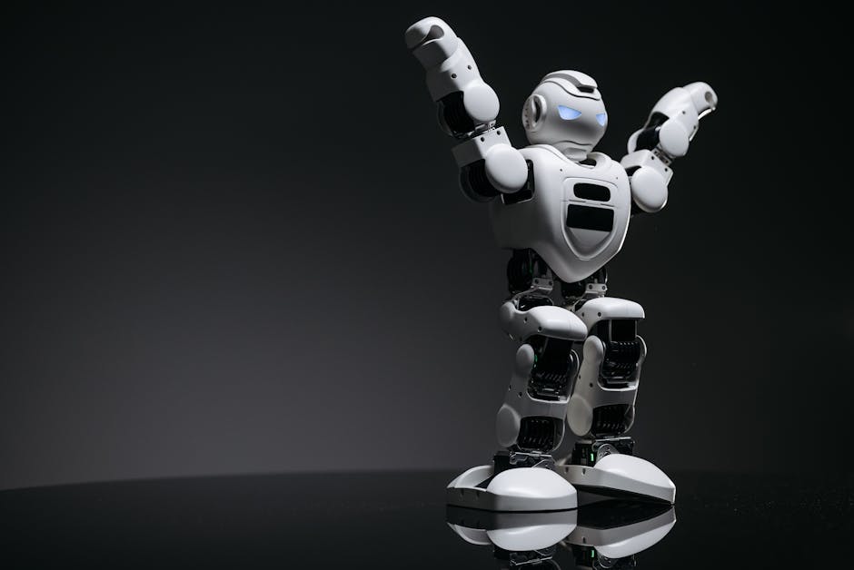 Close-up studio shot of a white robot toy with LED eyes raised in victory on a gray background.