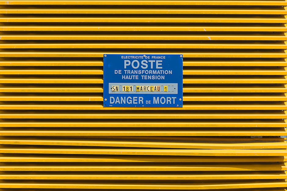 Close-up of a yellow industrial grate with a blue high voltage warning sign in French.