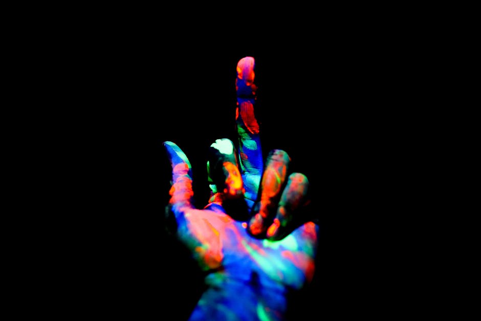 Crop anonymous persons hand painted with multicolored bright neon colors showing middle finger in obscurity