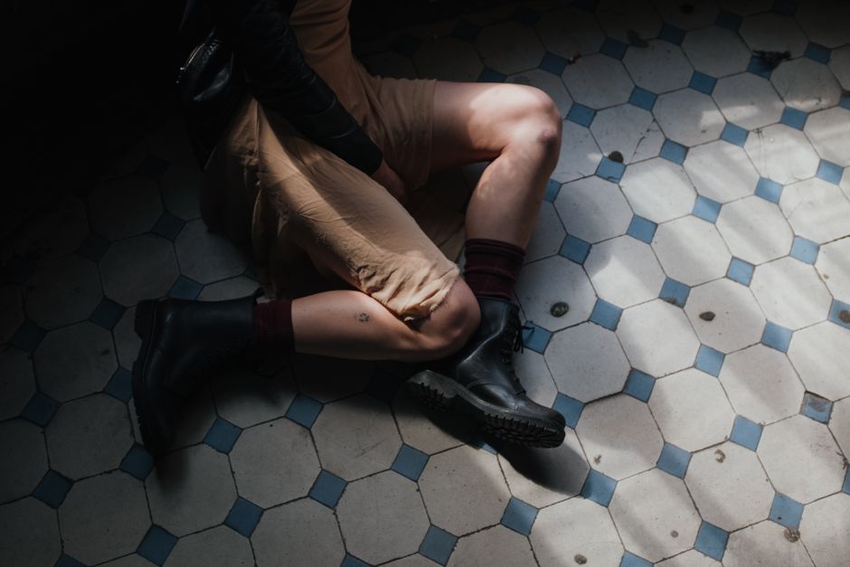 An artistic shot of a woman sitting on a vintage patterned tiled floor, showcasing fashion and style.