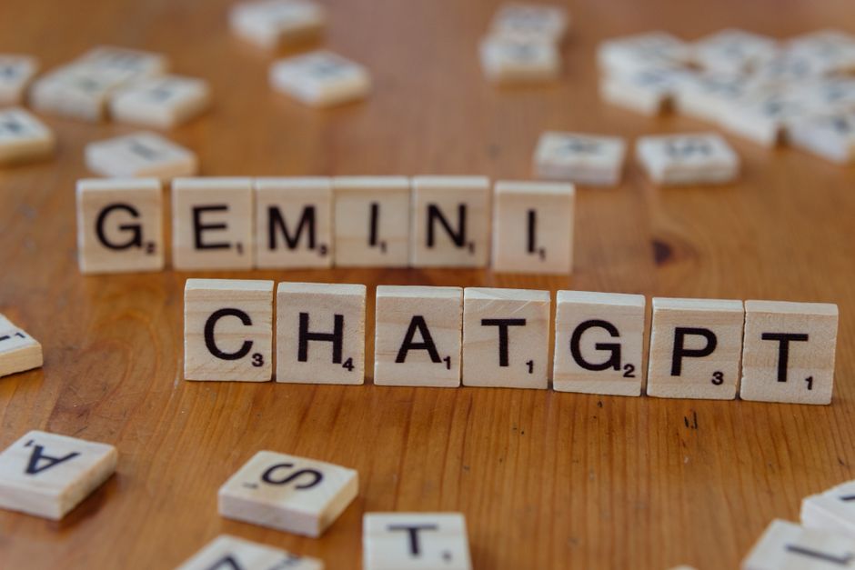 Close-up of wooden Scrabble tiles spelling Gemini and ChatGPT on a wooden surface.