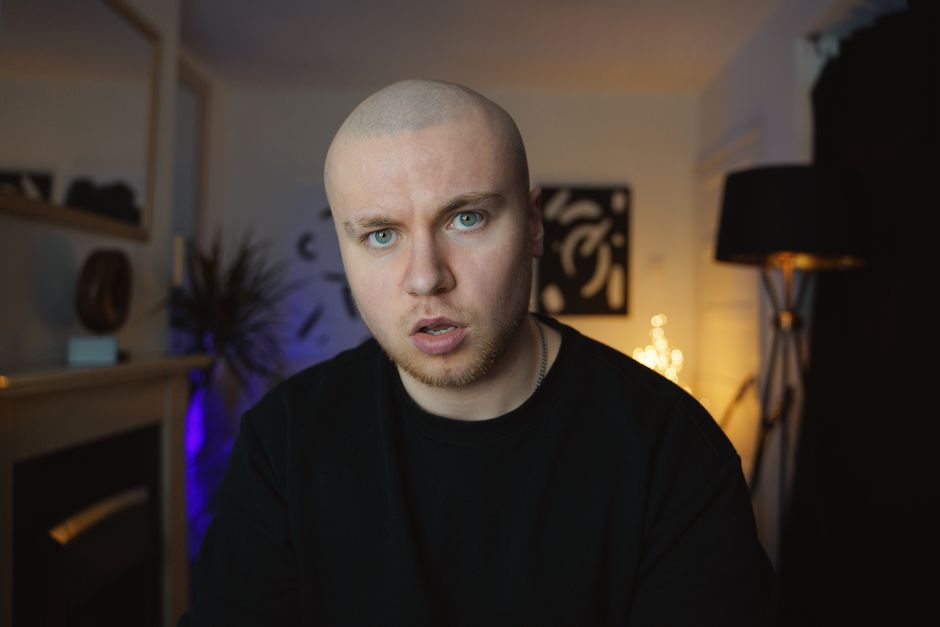 Bald man in casual wear sitting and vlogging indoors. Cozy home setting.