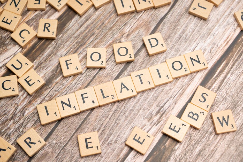 Wooden scrabble tiles arrange to spell 'Food Inflation' on a rustic wooden surface, conceptually depicting rising food prices.