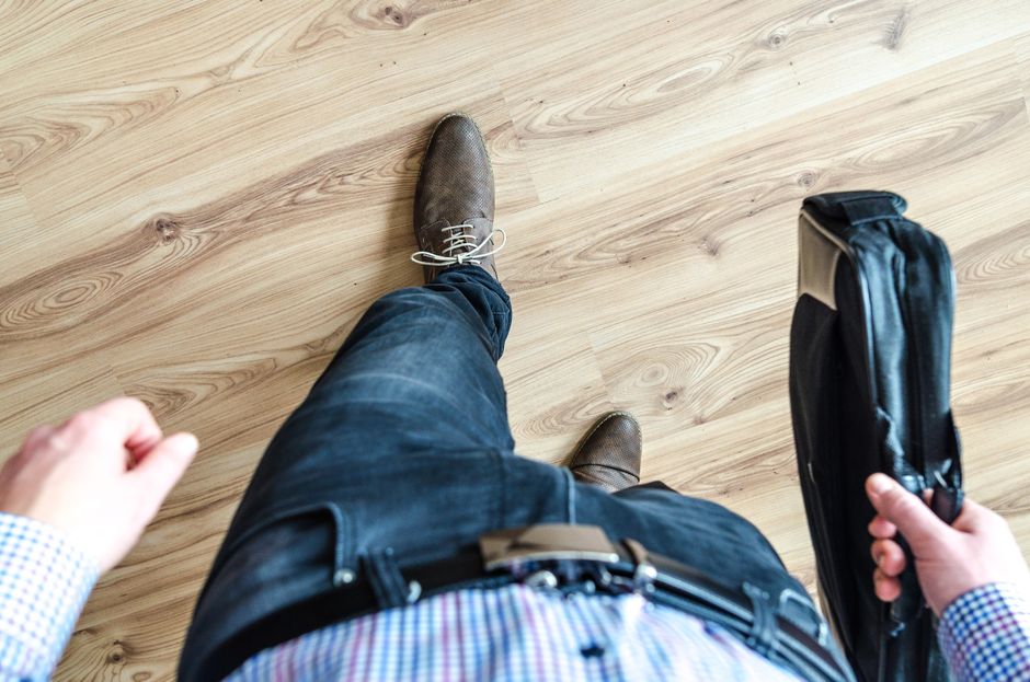 Overhead view of a businessman walking on a wooden floor holding a black briefcase.