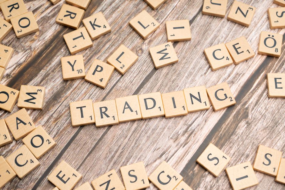 Wooden Scrabble tiles spelling 'TRADING' against a rustic wood background.